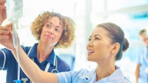 Two medical professionals preparing an IV infusion bag in a bright clinical setting
