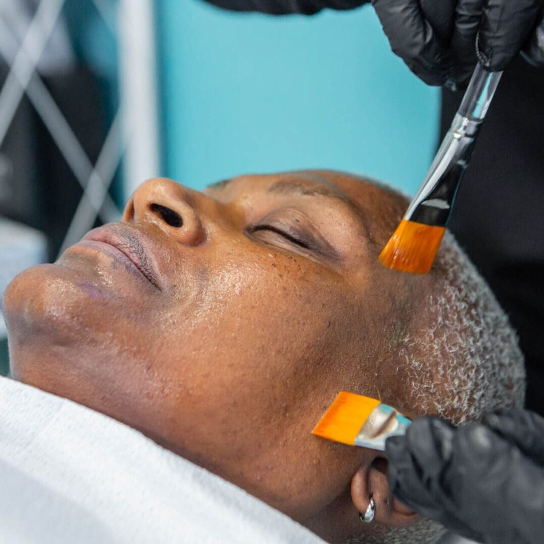 A person receiving a facial treatment with brushes and skincare products.