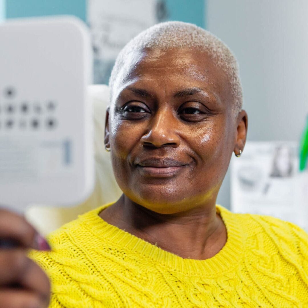 Smiling elderly woman with short gray hair wearing a yellow sweater.