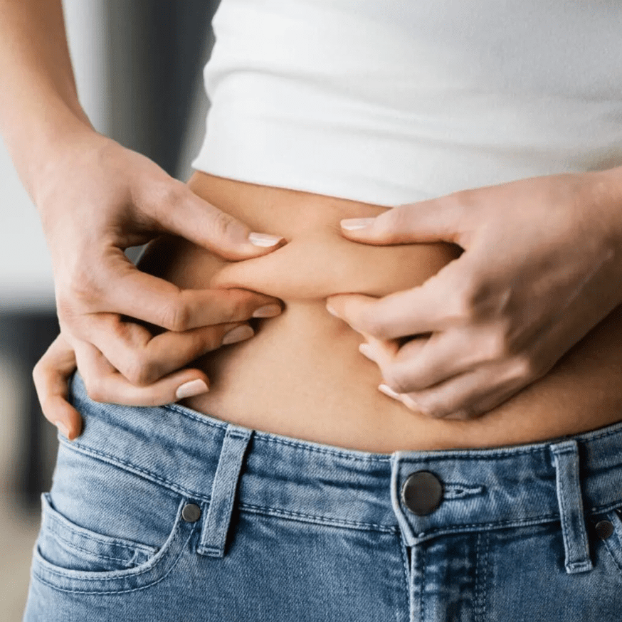 Person pinching belly fat while wearing jeans and white shirt.