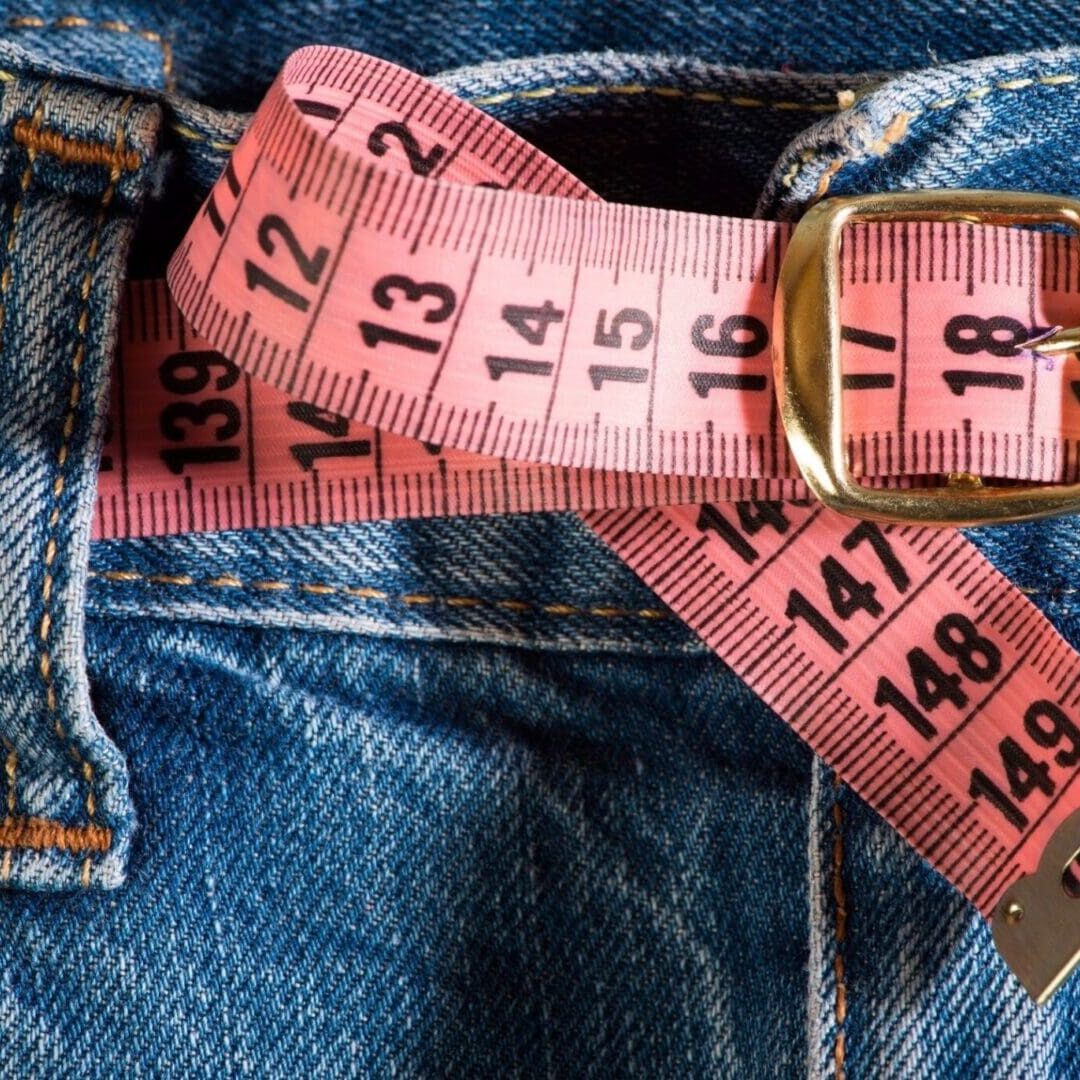A pink measuring tape tucked into a pair of blue jeans.